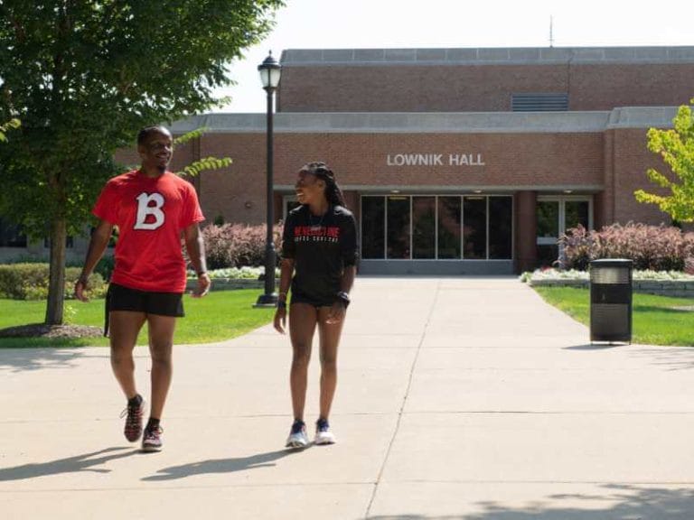 Two people walking down the sidewalk in front of a building.