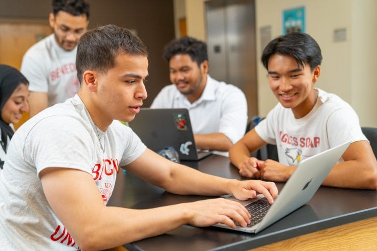 A group of students working on a laptop in a classroom.