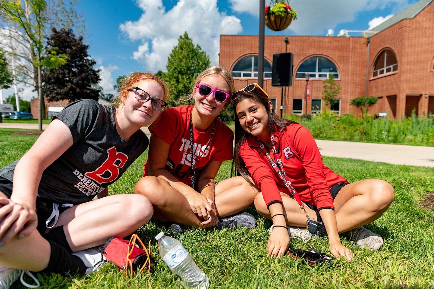 Three girls sitting on the grass in front of a building.